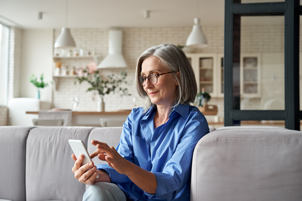 A woman at home, smiling as she reads through her options on her phone